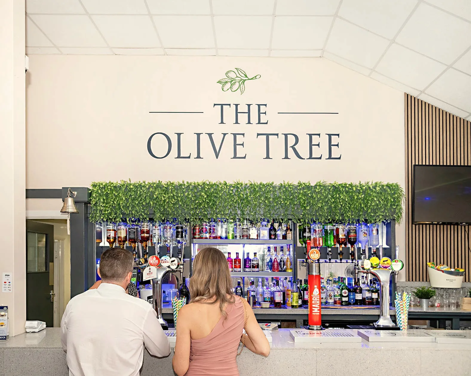 Two guests at the bar beneath The Olive Tree sign