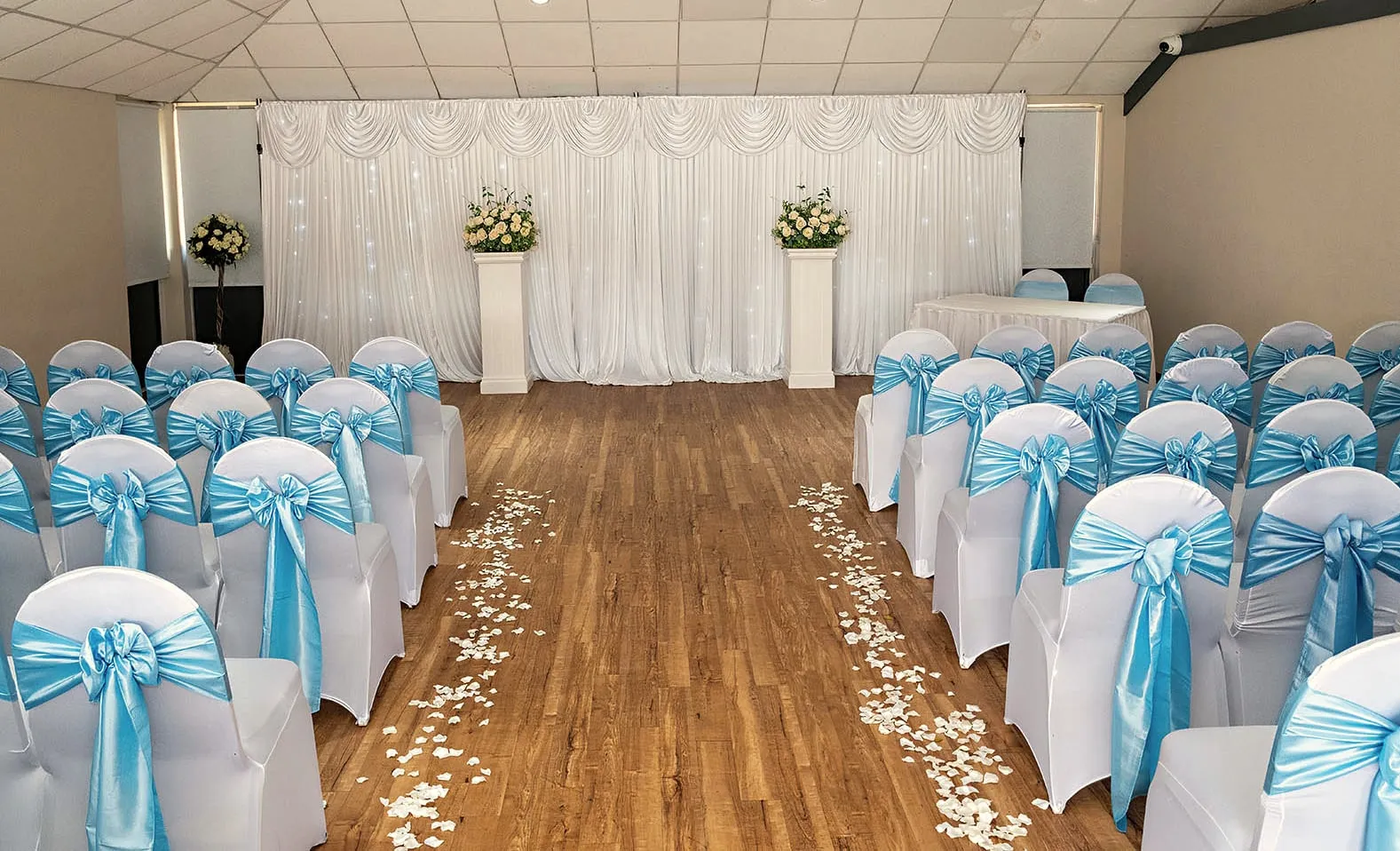 Ceremony room with white chair covers, pale blue sashes and a petal-strewn aisle