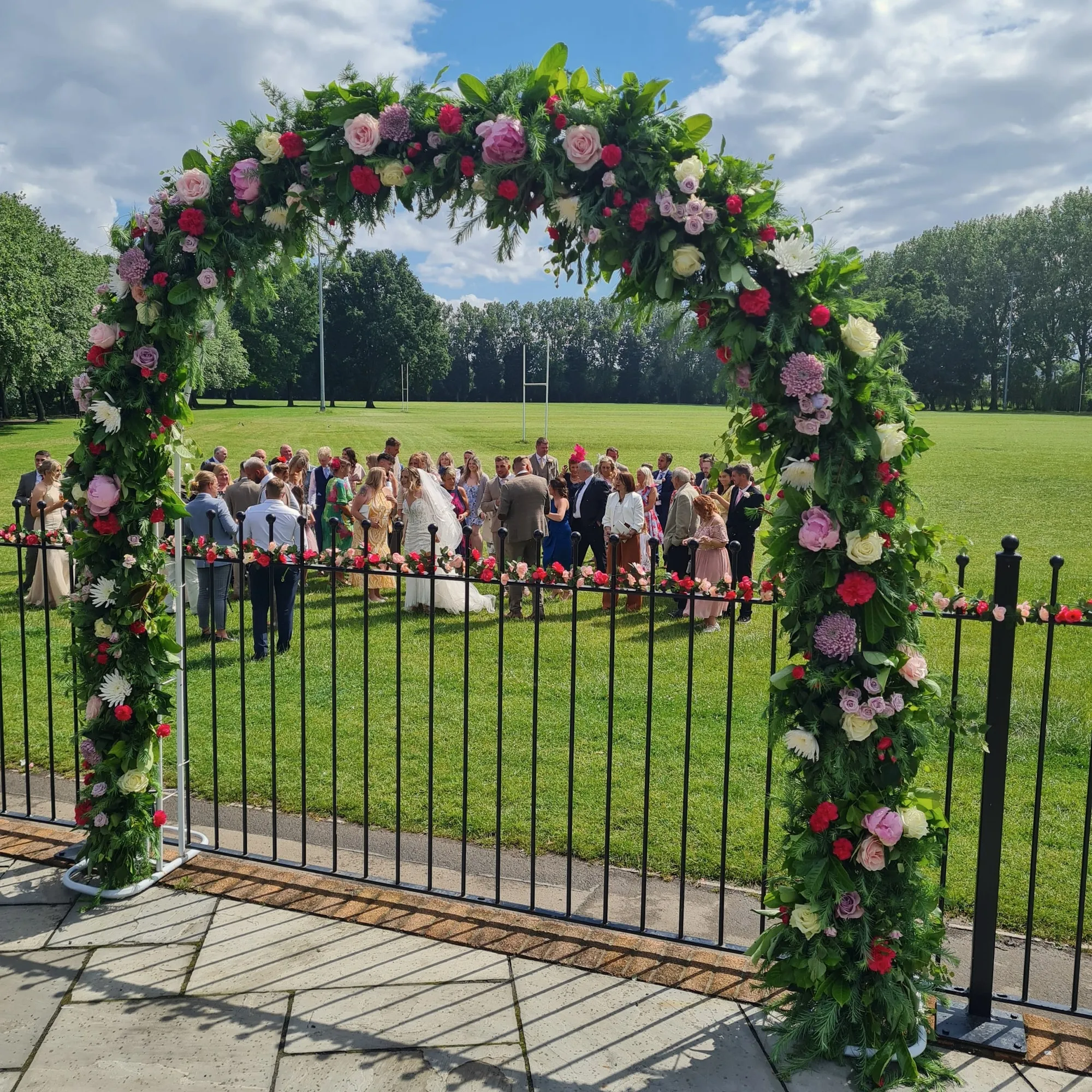 Rose arch on the patio with a wedding party gathered on the field beyond