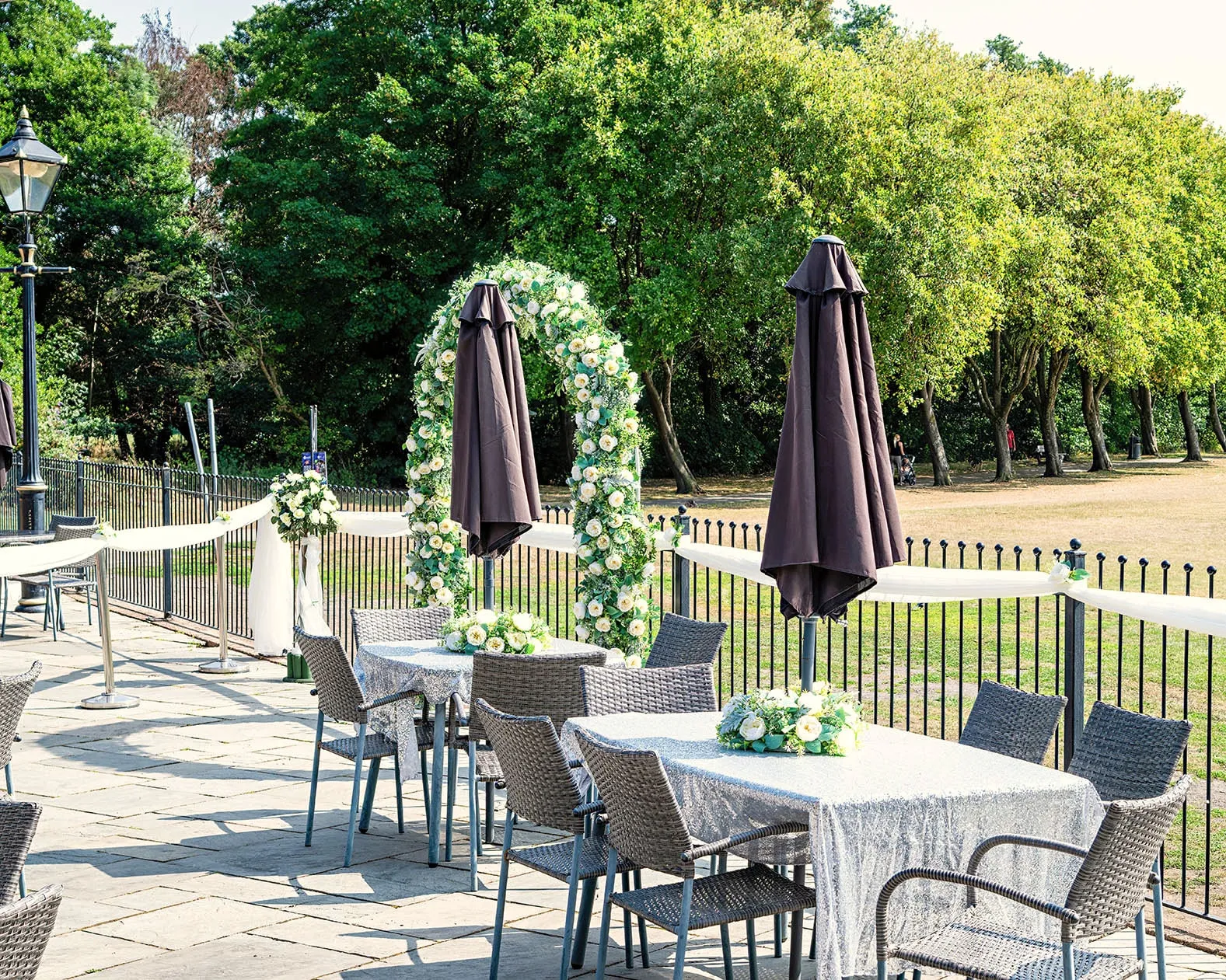 Floral arch and parasol tables on the patio, with trees and parkland beyond